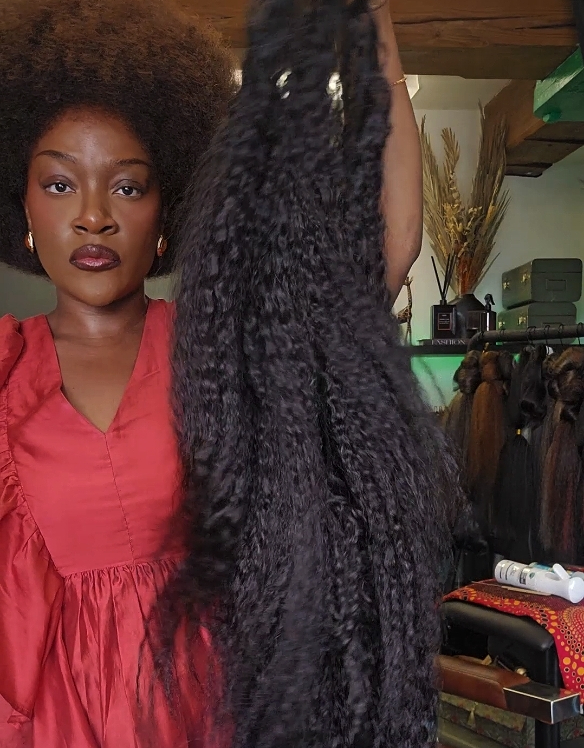 A woman holding up a long length of curly black weft hair